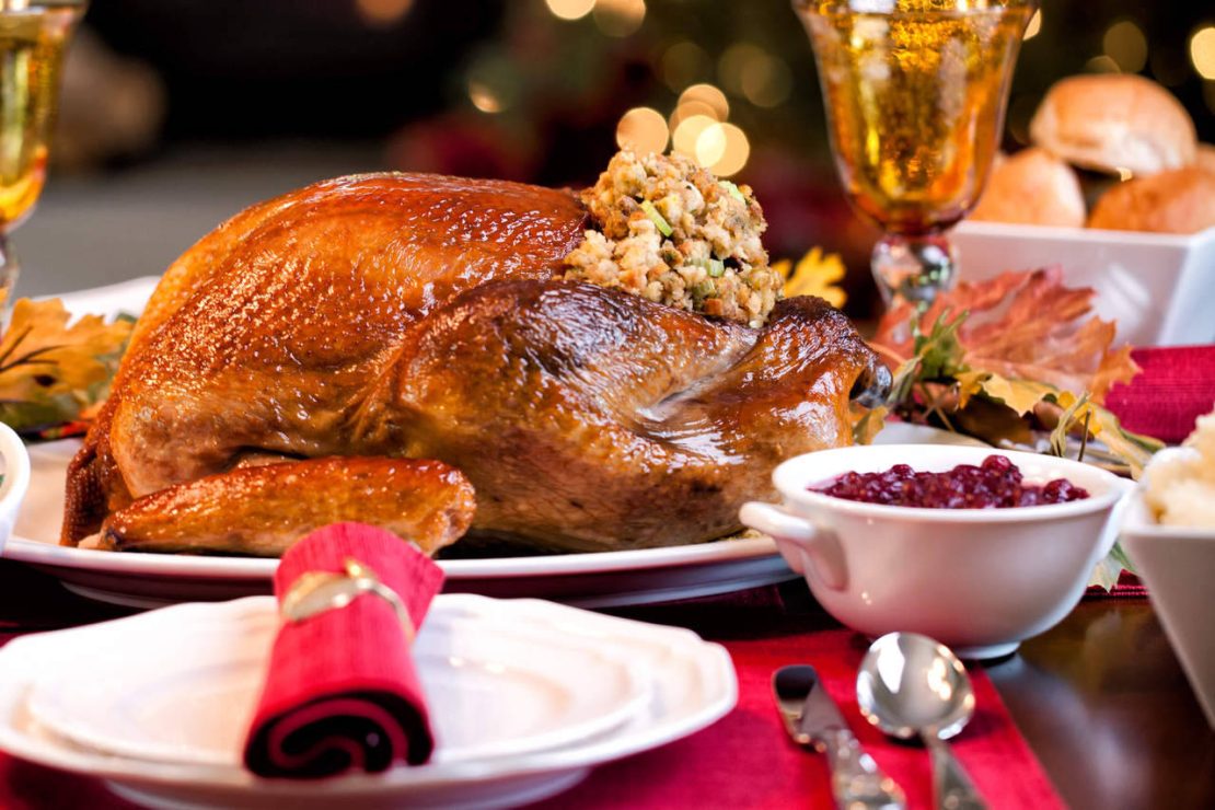 A roasted turkey stuffed with herbs on a platter, surrounded by carrots and greens, on a wooden kitchen counter.