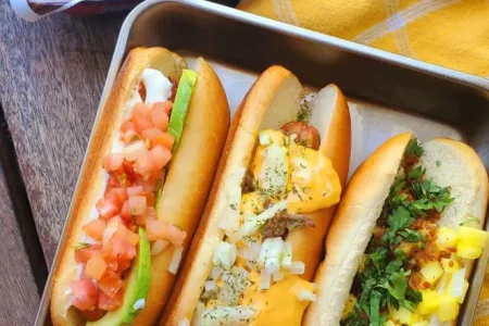 franks-662x1024 Grilled turkey franks topped with variety of vegetables placed in a metal tray.