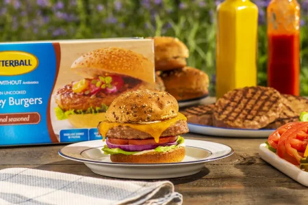 Turkey burgers with tomatoes, onion, lettuce and melted cheese placed on an outdoor table.