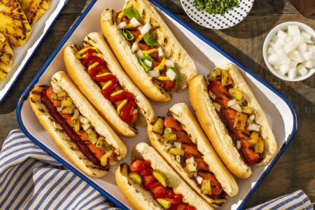 TURKEY-FRANKS-WITH-BBQ-SAUCE-051-1x1-1 Turkey franks hot dogs placed topped with grilled vegetables placed in a tray.