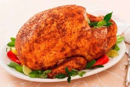 RoastTurkeySpicyRub A roasted turkey stuffed with herbs on a platter, surrounded by carrots and greens, on a wooden kitchen counter.